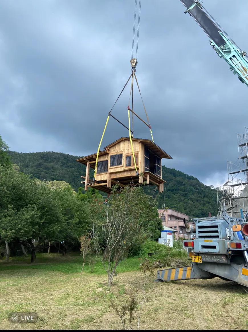 吊車將一整棟木屋整棟吊起準備遷移，背景為南投山林